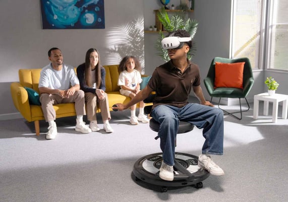 A teen boy wearing a VR headset sits in a Roto VR Explorer chair while his family looks on.