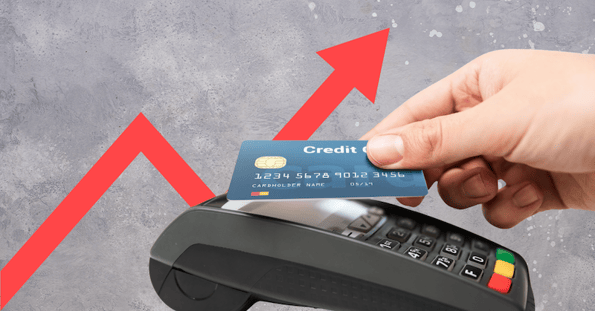 A hand taps a credit card to a payment machine in front of a rising red arrow against a gray background. 