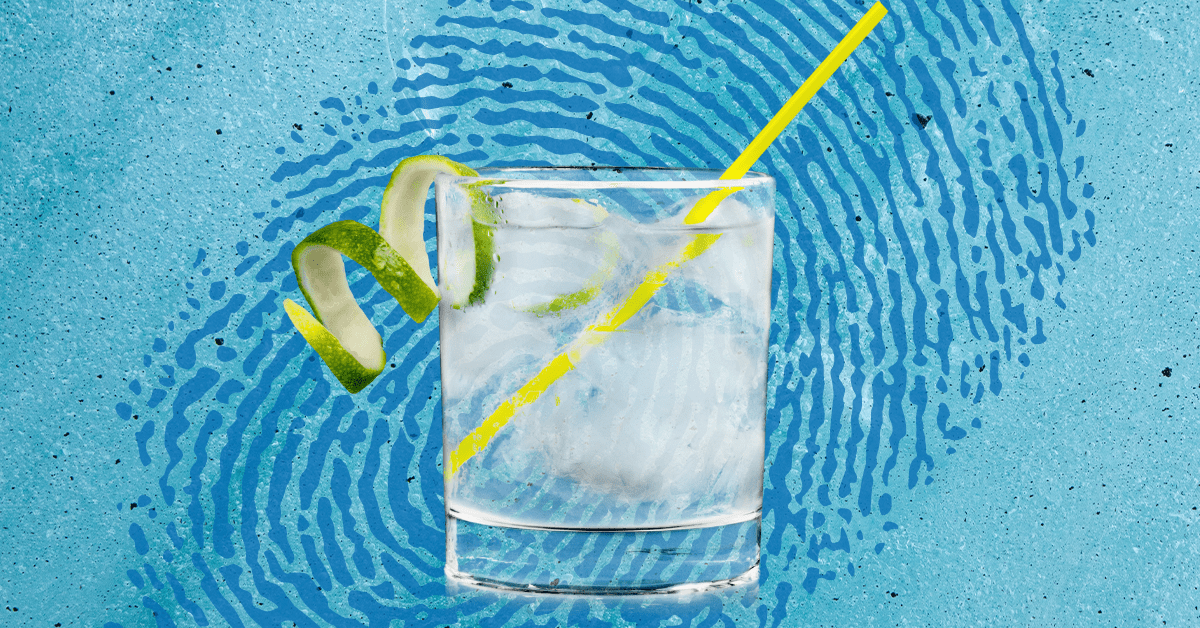 A gin cocktail in a clear glass with a yellow straw and lime garnish on a blue background with a blue fingerprint.