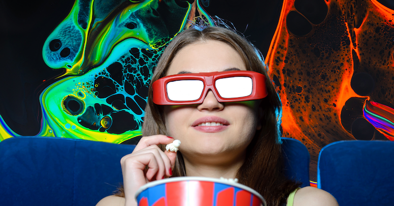 A woman wearing glasses eats popcorn in a movie theater.