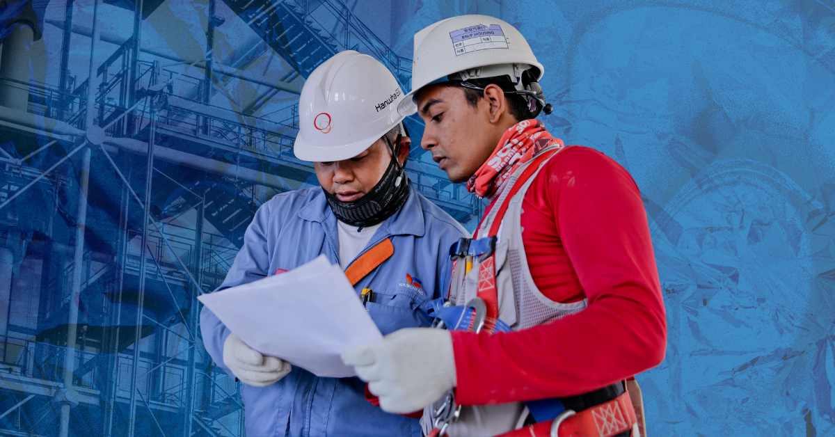 Two men in white hard hats and construction gear looking at a piece of paper.